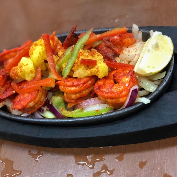 Sizzling Indian shrimp dish with red and green bell peppers, onions, cauliflower, and a lemon wedge.