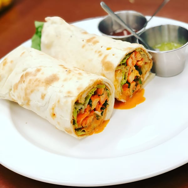 Two Indian chicken wraps with lettuce and orange sauce, served with two dipping sauces.
